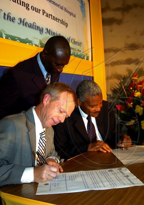 Winston Sill / Freelance Photographer
Andrews Memorial Hospital and Florida Hospital host function in Celebration of Partnership and Signing of Agreement, held at Andrews Hospital Complex, Hope Road on Thursday August 12, 2010. Here  Lars Houmann (left), President and CEO, Florida Hospital; Dr. Patric Rutherford (right), President, Andrews Memorial Hospital signing the agreement. Looking on is Paster Derek Bignall, Chairman, Andrews Memorial Hospital.