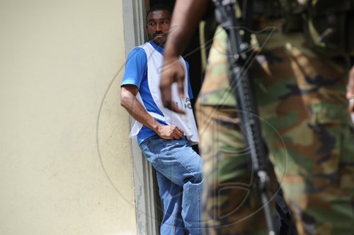 Ricardo Makyn/Staff Photographer
An Election Day worker looks on while a JDF Soldiers Stands by in Troja at the By-election in N.E. St. Catherine