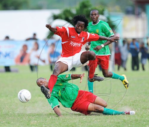 Ricardo Makyn/Staff Photographer.
August Town's Terrence Shaw leaps over a challenge from Humble Lions' Dion Sterling during their National Premier League play-off match at the Mona Bowl yesterday. The match ended 0-0. Sterling's teammate Keveral Stewart looks on.