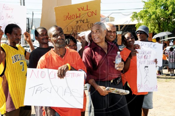 Norman Grindley /Chief Photographer
Opposition spokesman on Finance, Dr Omar Davies, at second from right with water bottling in hand, is fully enjoying the ?shaded? protection of a band of ?no taxMas? protesters gathered at Mandela Highway in Kingston on Wednesday, December 23, 2009, to voice opposition to the new $21.8 billion tax package announced December 17 by the Bruce Golding Administration. The protest was organized by the People?s National Party, who have called the measures ?wicked and unsconsionable? because of its expected impact on lower income groups.